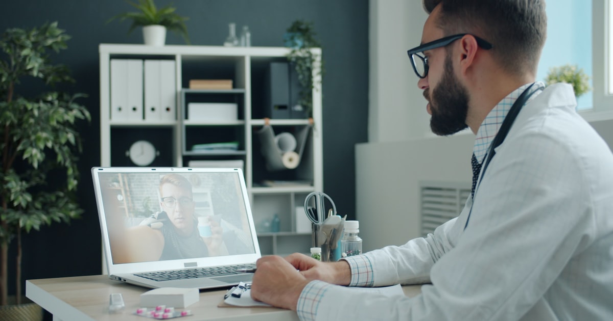 Médico de jaleco fazendo teleconsulta por vídeo chamada no notebook, em consultório