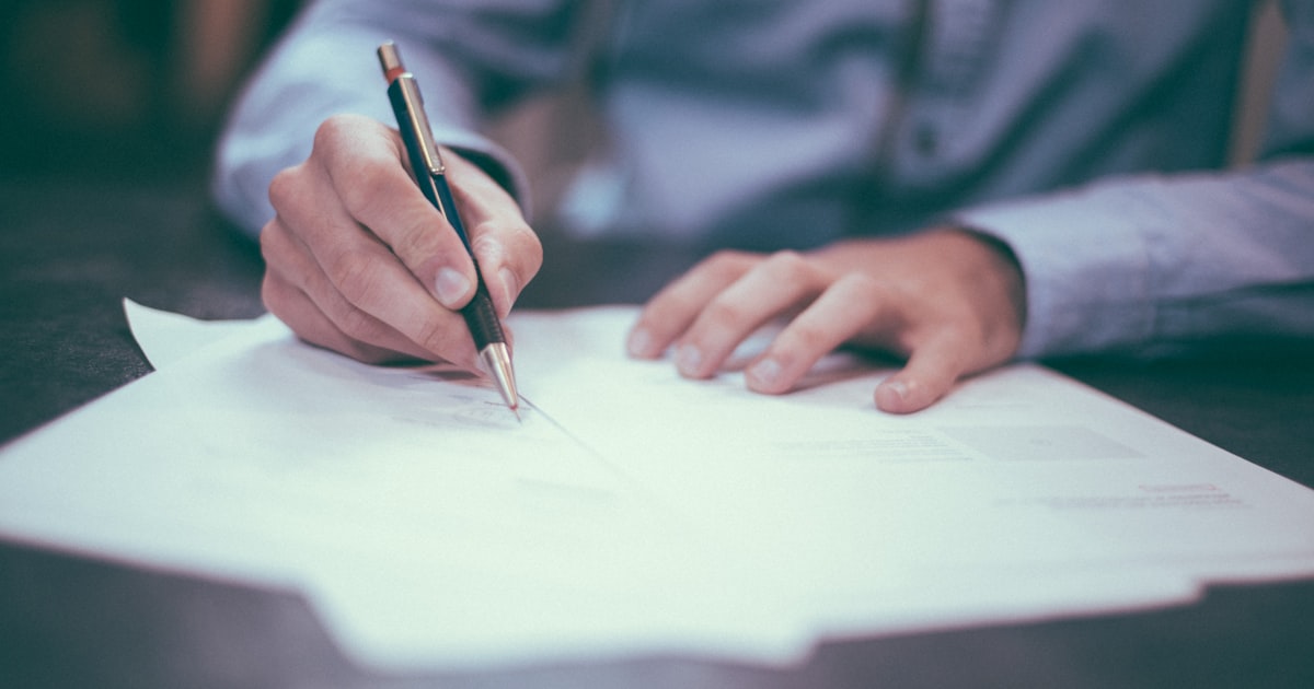 Mão anotando números em um documento, representando a análise financeira do consultório