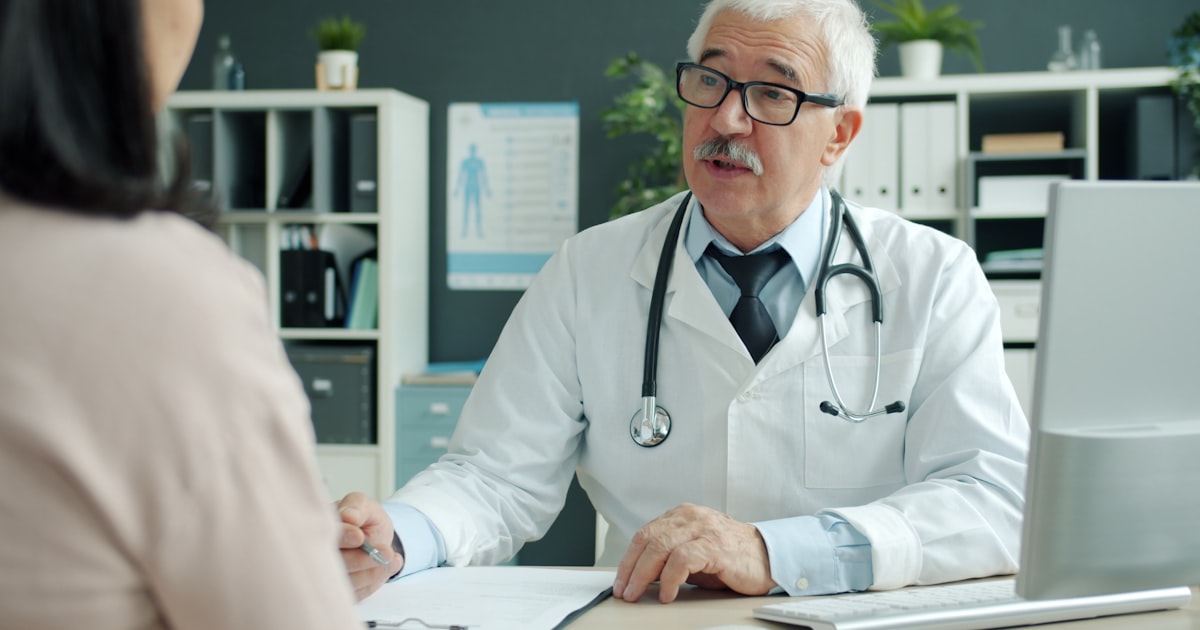 Médico conversando com paciente durante a consulta, em close das mãos sobre a mesa